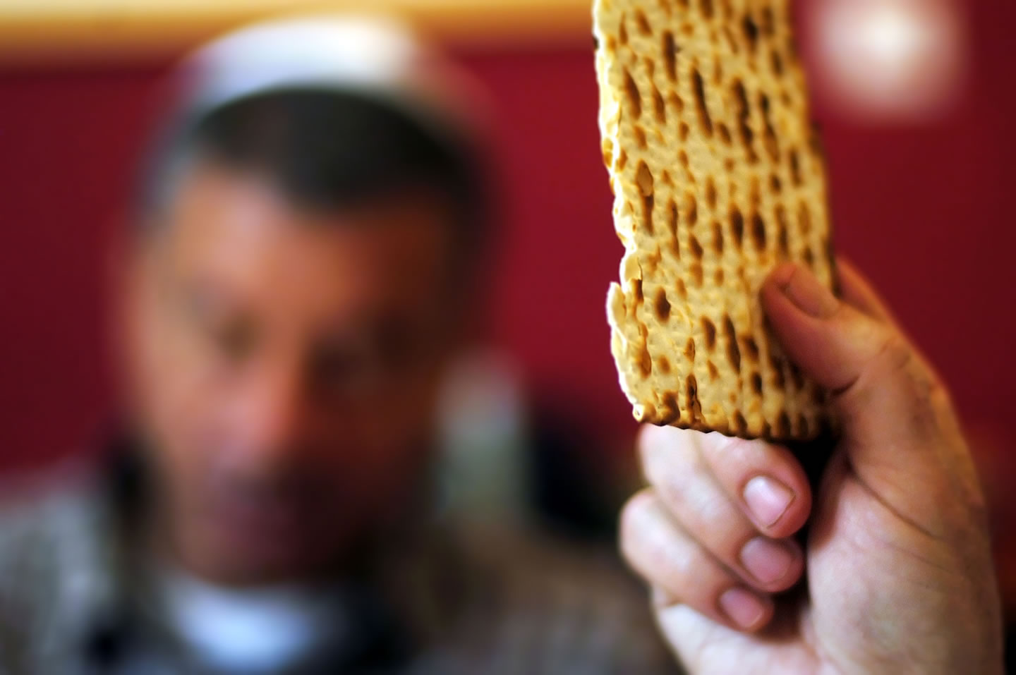 burry person in background with a hand holding piece of matzah in the foreground